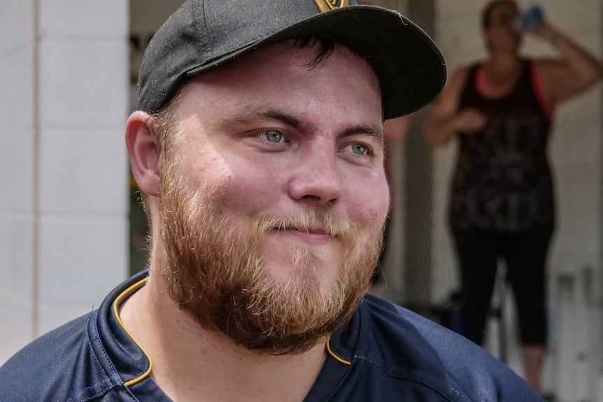 A man with a baseball cap and facial hair stares off to the side.