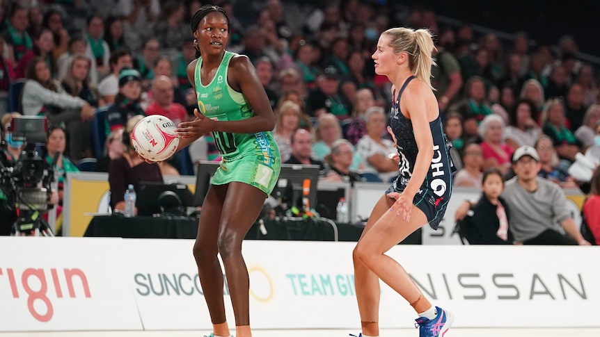 A West Coast Fever Super Netball player holds the ball while under defensive pressure from a Melbourne Vixens opponent.