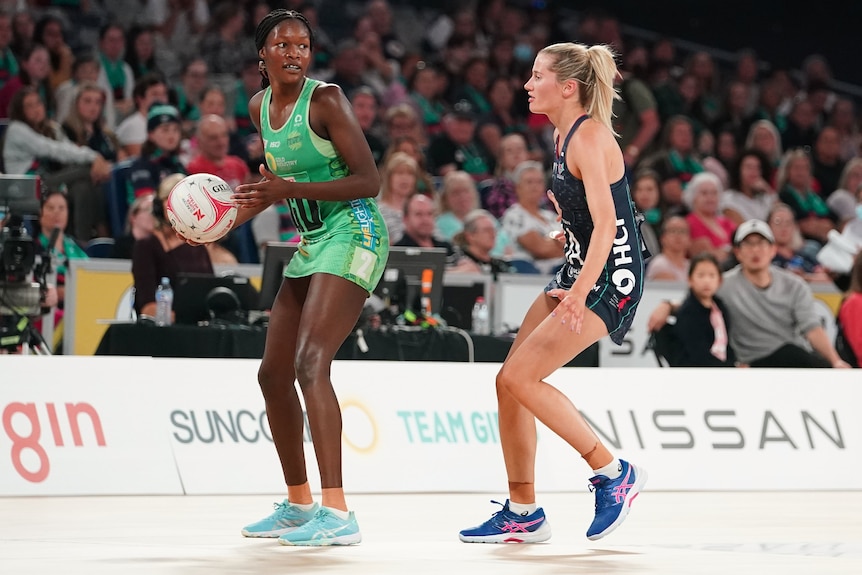 A West Coast Fever Super Netball player holds the ball while under defensive pressure from a Melbourne Vixens opponent.