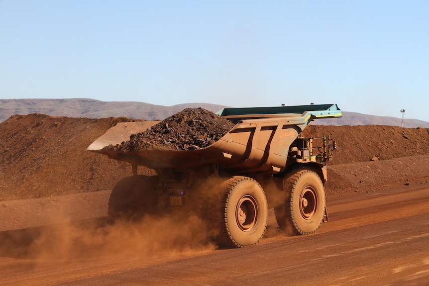 A large truck carrying iron ore drives up a hill