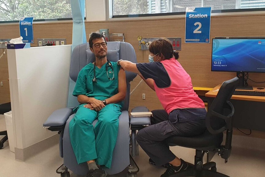 A man in green scrubs receives the COVID-19 vaccination at Coffs Harbour Health Campus.