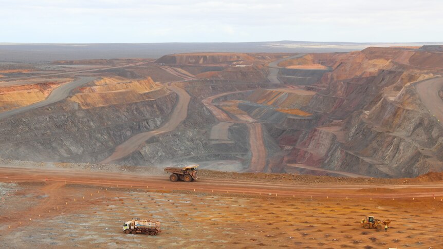 landscape view from lookout of open cut mine with layers of cuts and a truck, water truck, digger and ute down below on site
