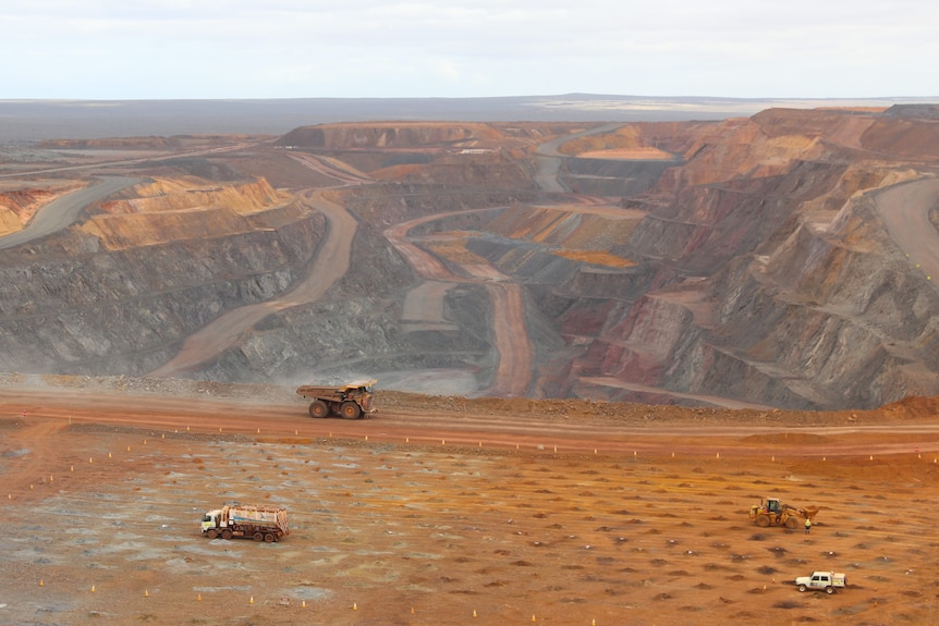 landscape view from lookout of open cut mine with layers of cuts and a truck, water truck, digger and ute down below on site