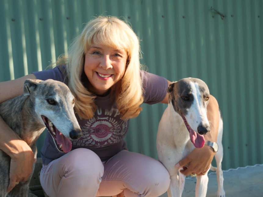 Annie Hendley with her arms around two greyhounds.
