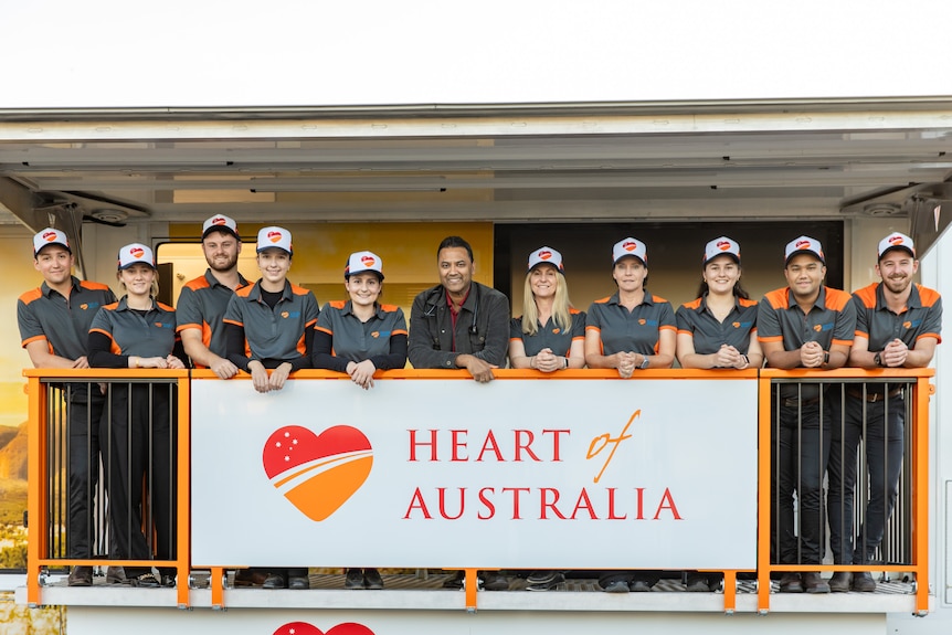 A group of people leaning on a balcony with a sign attached to the rail that says Heart of Australia