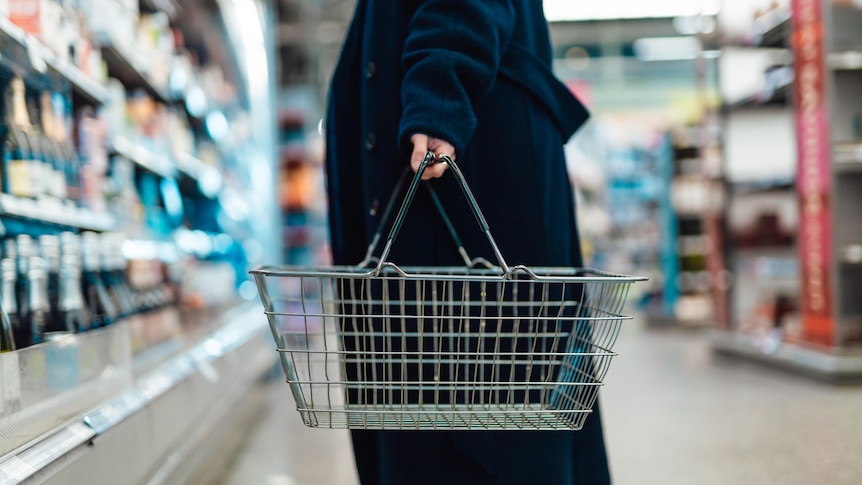 Cropped shot of young woman carrying shopping basket, standing at produce aisle in supermarket.