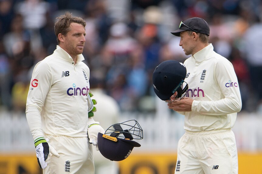 Jos Buttler stands with his arms by his side talking to Joe Root, both holding batting helmets