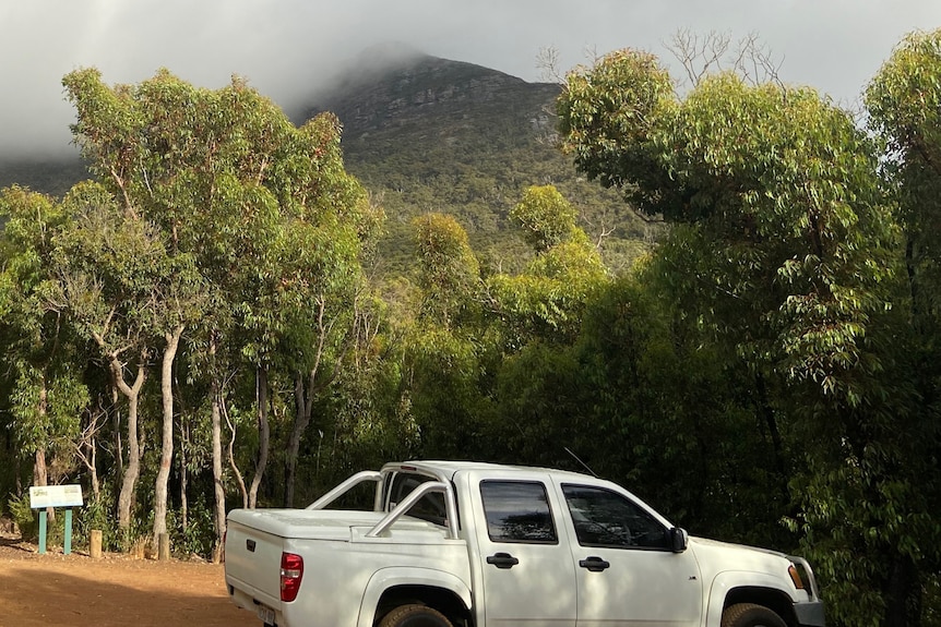 a white Holden Colorado utility parked in a dirt car park surrounded by bush with a mountain in the background