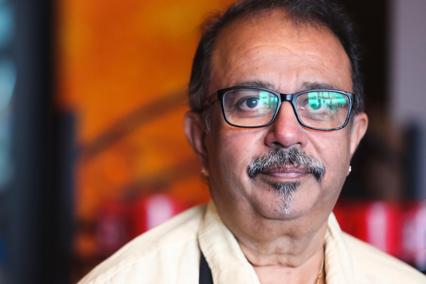 A close-up portrait of a man wearing glasses and looking directly ahead.