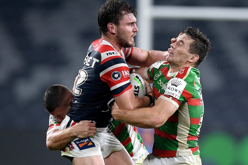 A Sydney Roosters NRL player attempts to palm off a South Sydney opponent with his left hand.