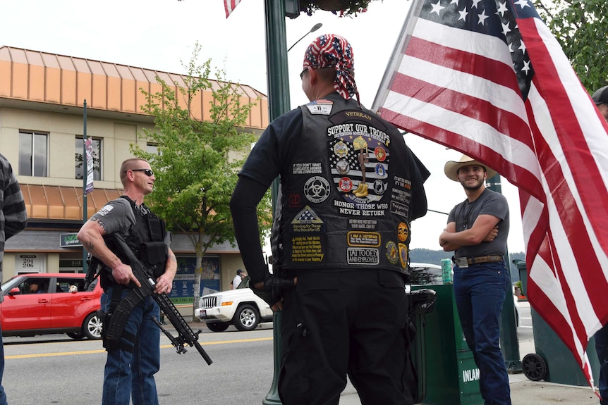 Men in tactical gear and holding huge guns chat on a street corner