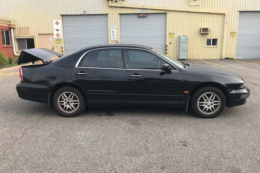 A black sedan with its boot open in front of a large shed