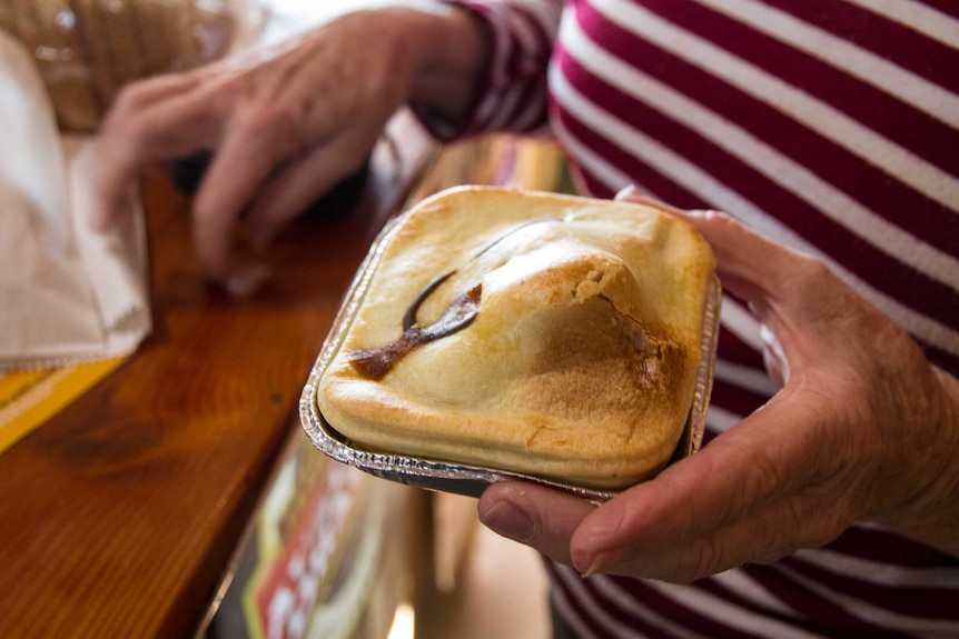 A woman hold a camel pie which has a pastry bubble that makes it look like it has a hump