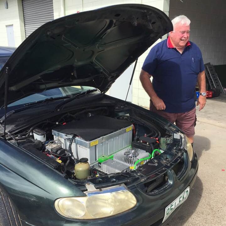 An elderly man beside a car with popped bonnet showing an electric motor
