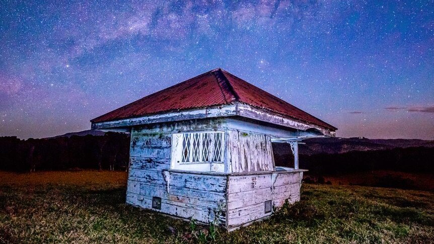 A dilapidated hut under a very starry night sky.