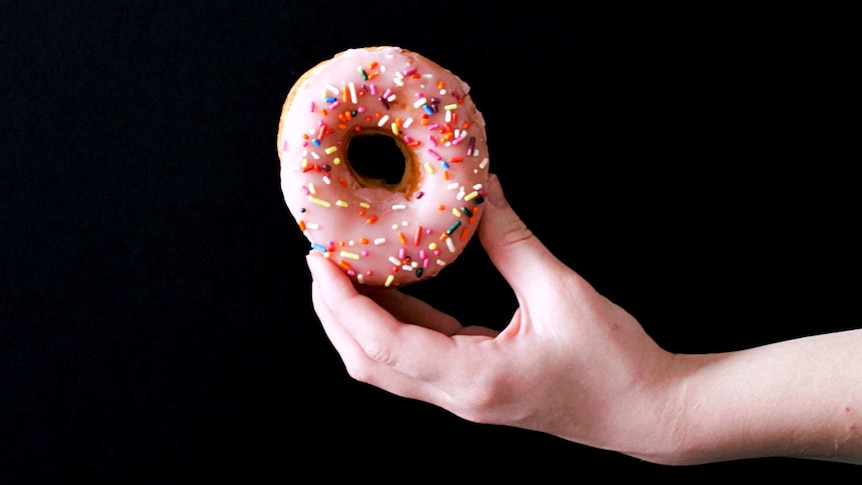 A hand holding up a pink donut with sprinkles