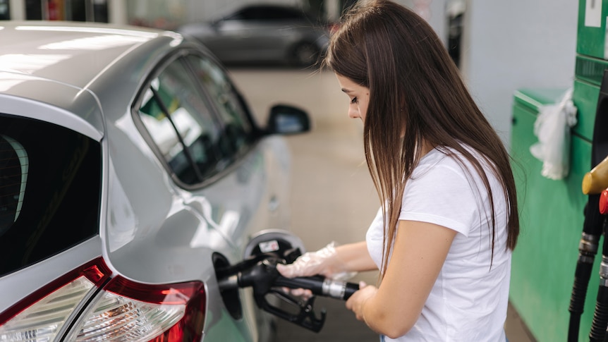 Stock image of a woman filling up her car at a petrol station with petrol.