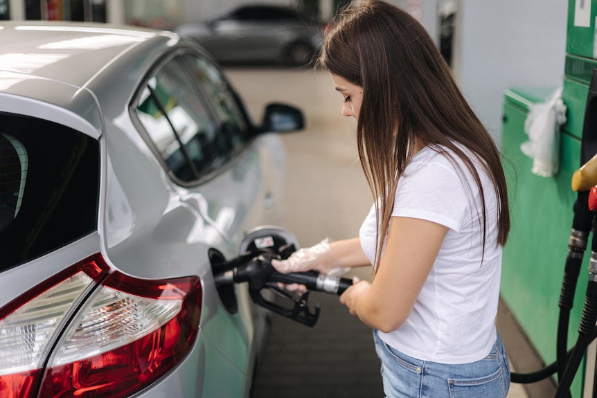 Stock image of a woman filling up her car at a petrol station with petrol.