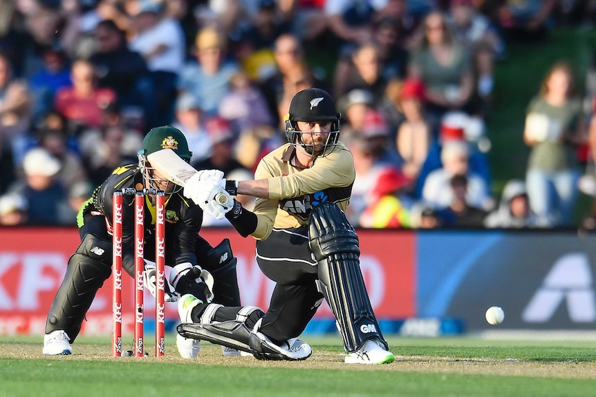 A NZ cricketer gets down on one knee to sweep the ball in a T20 International against Australia.
