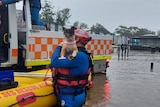 An emergency services worker stands in floodwater, holding a dog.
