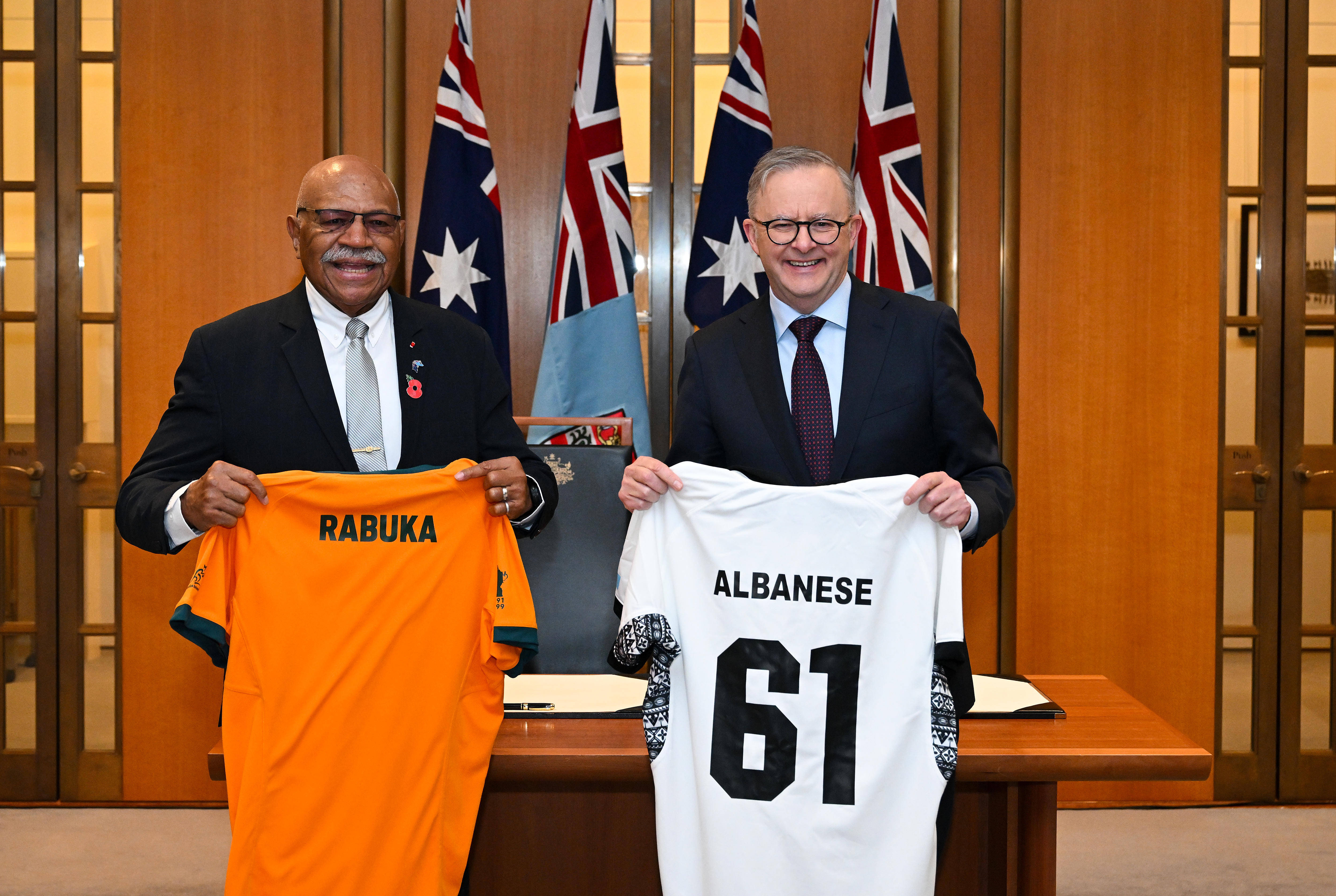 Two men wearing suits hold up rugby jerseys next to each other