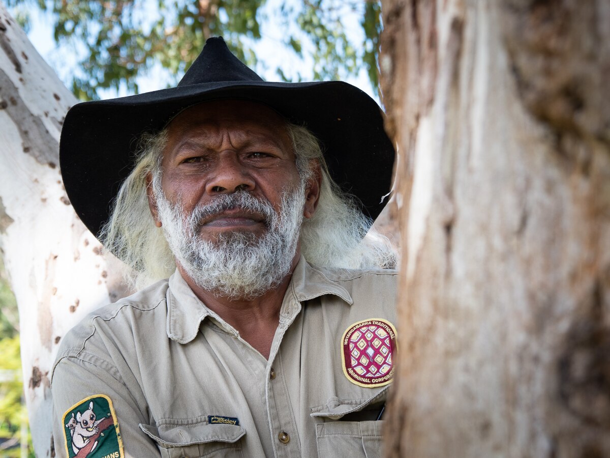 Indigenous man wearing large hat standing by tree
