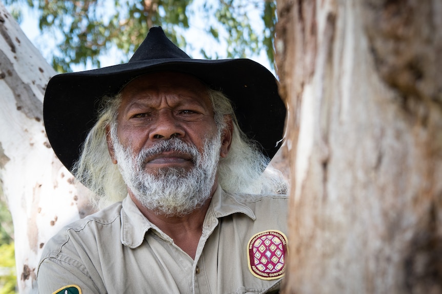 Indigenous man wearing large hat standing by tree