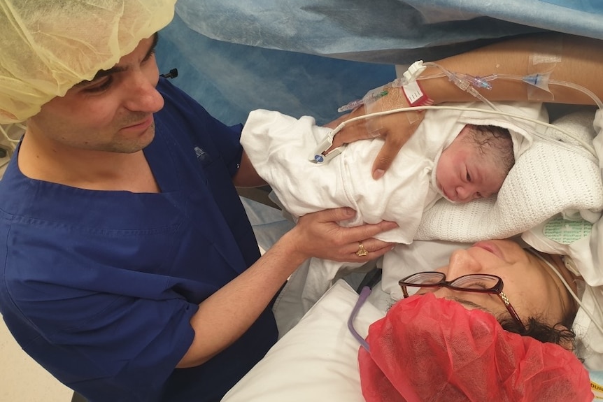 A woman holds a newborn baby with her husband nearby in the operating theatre.