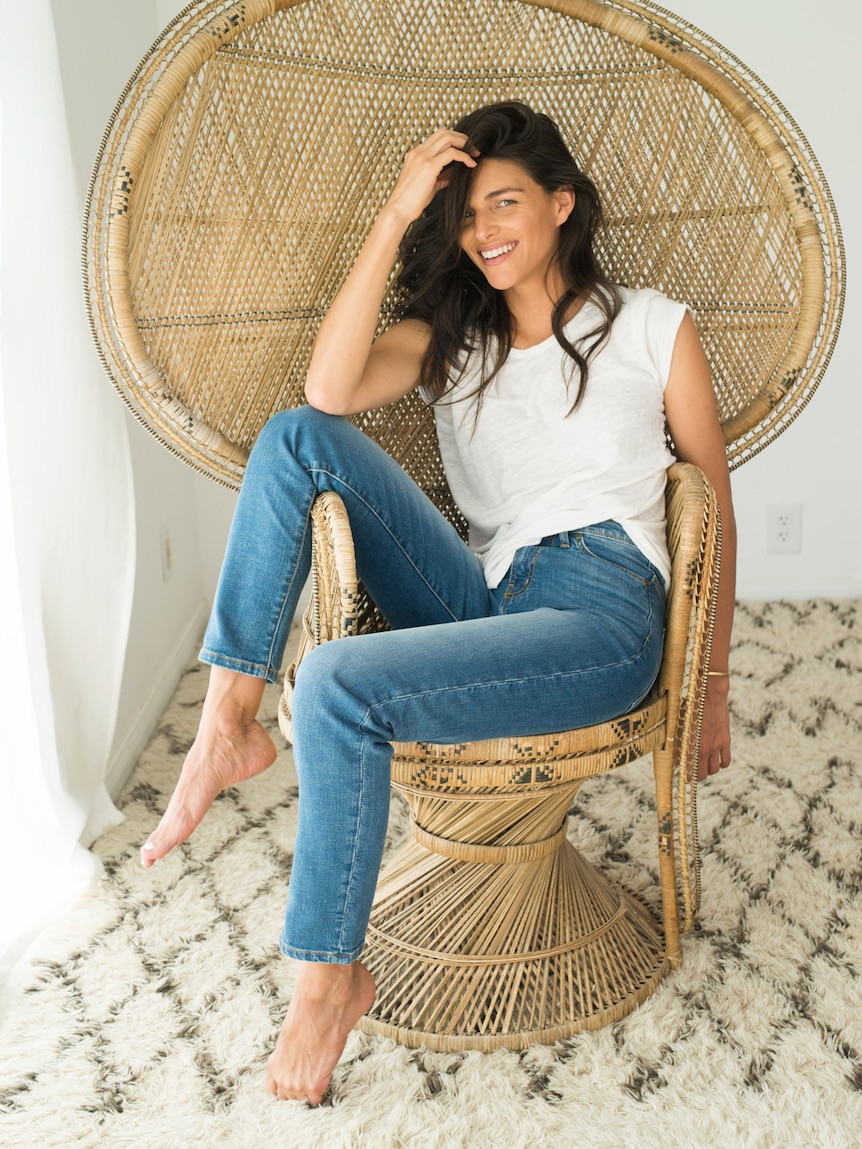 Lady wearing blue jeans sitting in a wicker chair.