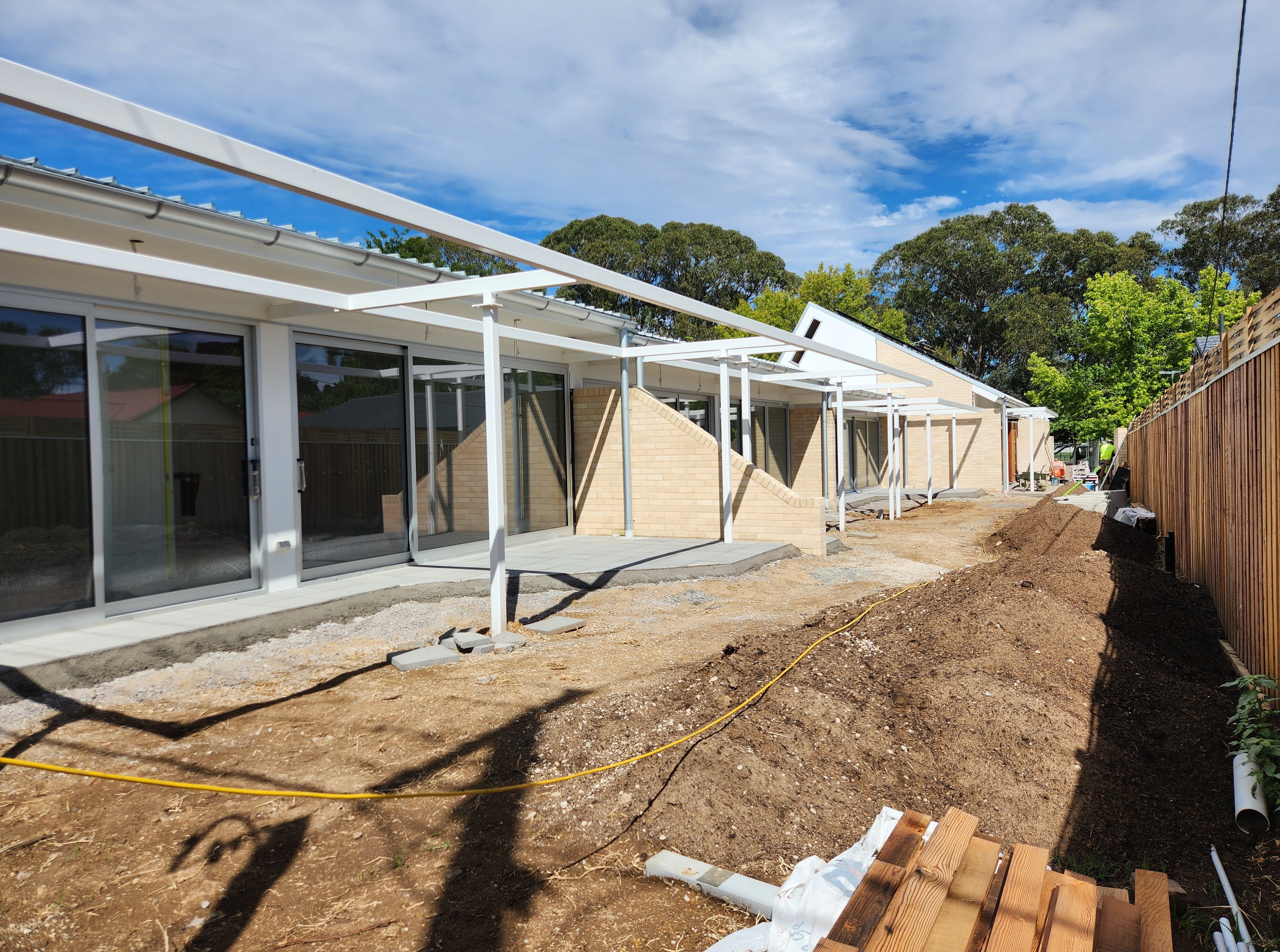 A long building of residences is partially built, dirt on the ground instead of grass.