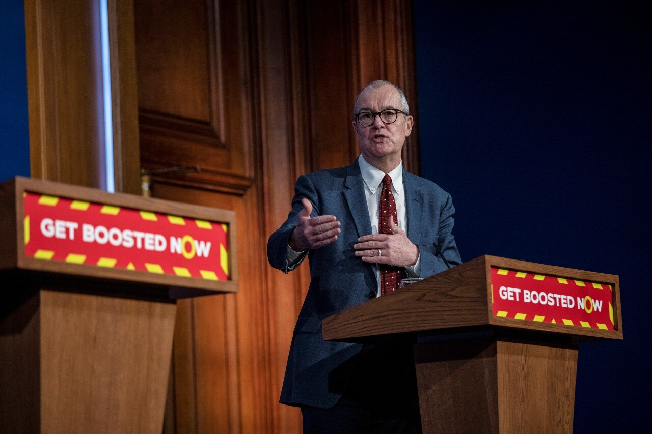 A man in a suit speaking and gesturing with his hands behind a lecturn