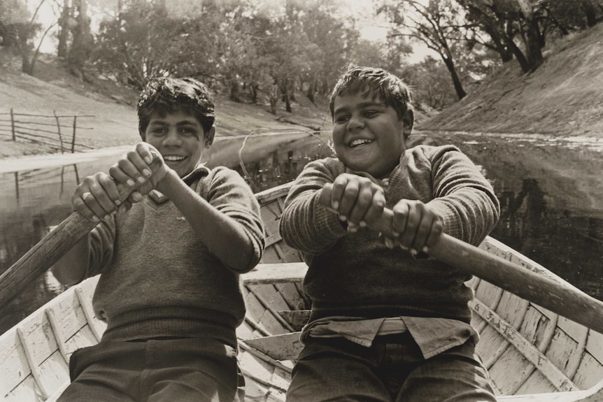 Two young boys rowing a boat.