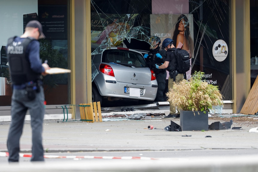 La polizia ispeziona un'auto d'argento che si è schiantata contro un pedone e la vetrina di un negozio