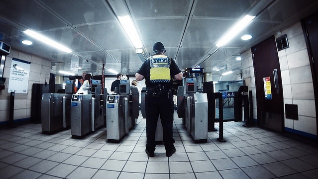 Police office stands with his back to the camera at train station in London.