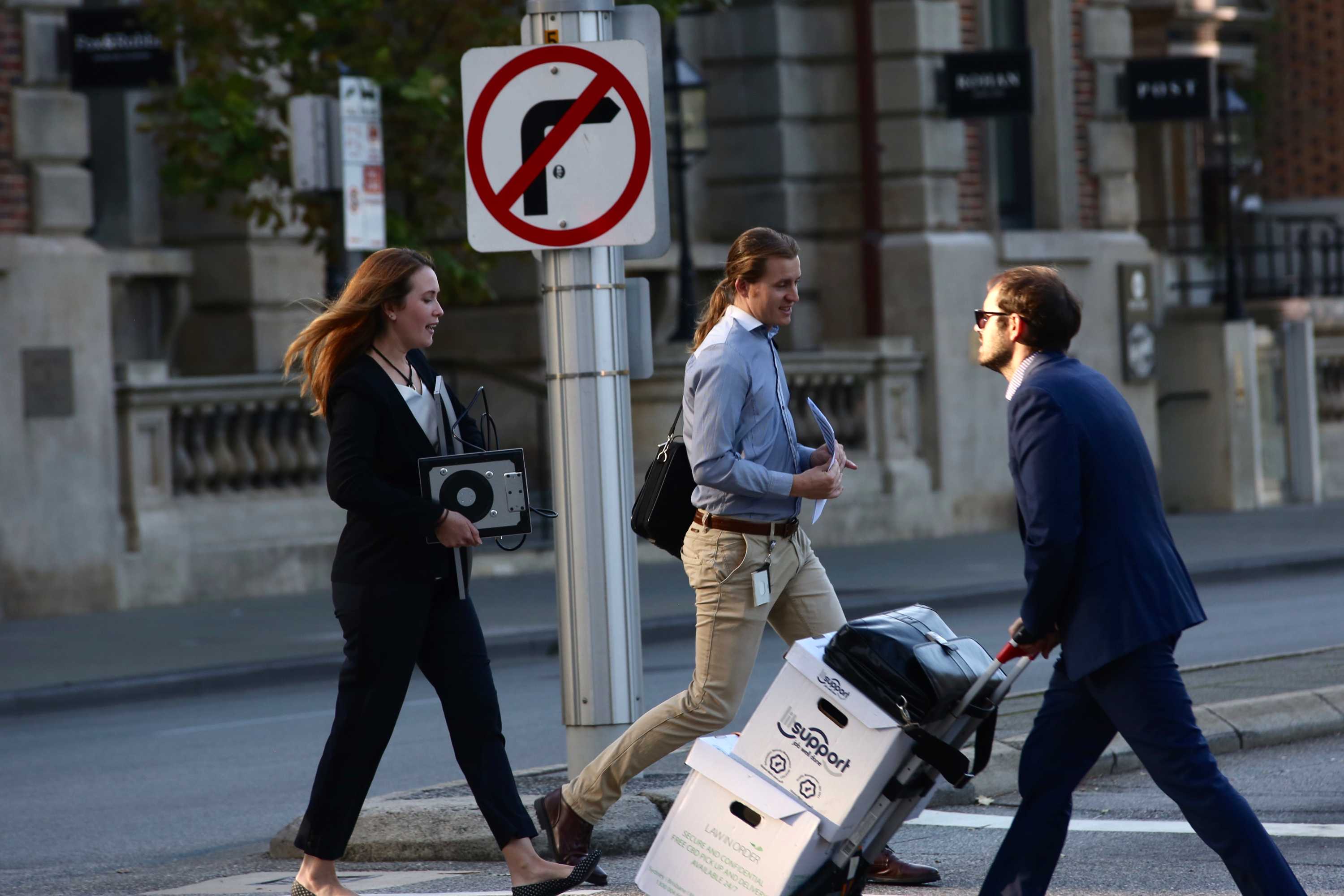 Two men and a woman in business attire cross the road in Perth's CBD. The woman carries a monitor.