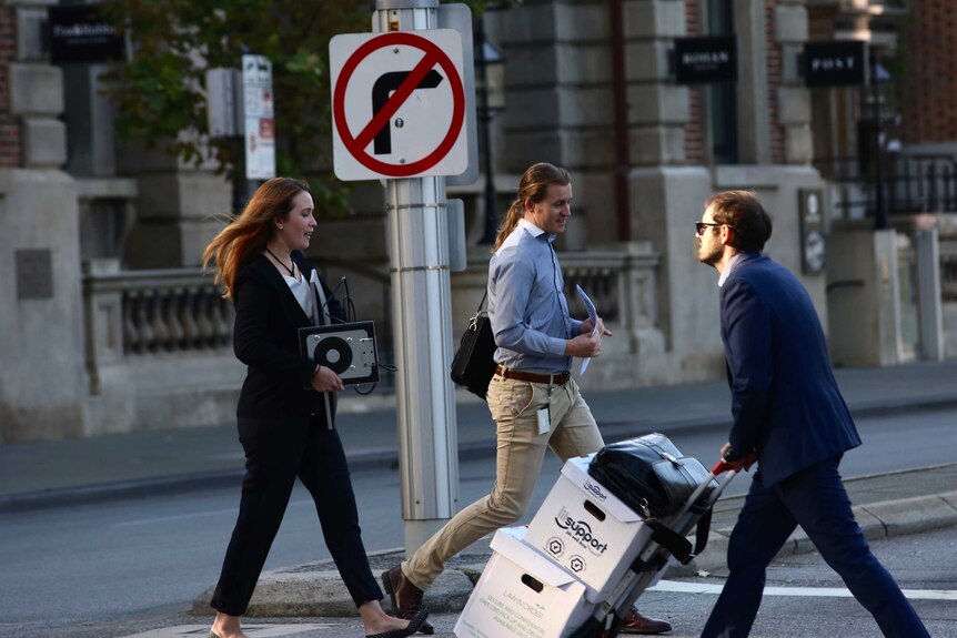 Two men and a woman in business attire cross the road in Perth's CBD. The woman carries a monitor.