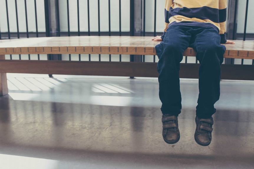 An unidentified child sits alone on a bench.