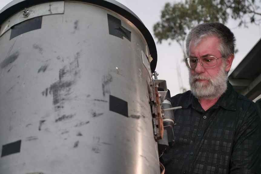 A man with a grey hair and glasses looks at a large telescope.