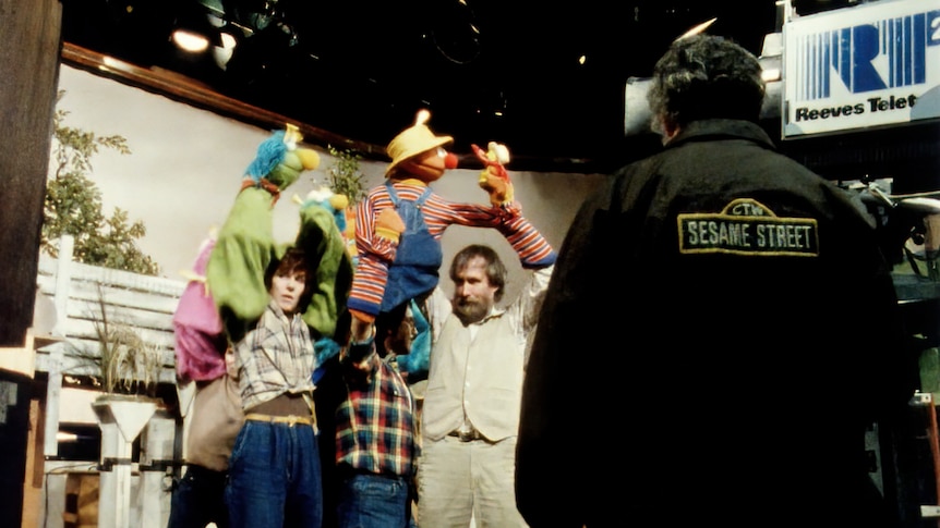 Two puppeteers perform in a TV studio. Crew member in foreground.