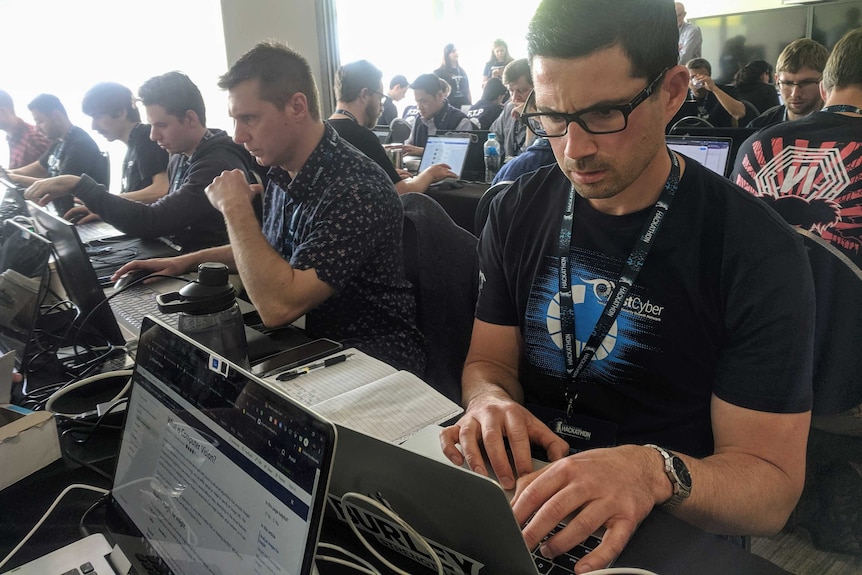 A man looks intently at a computer screen in a room full of people doing the same.