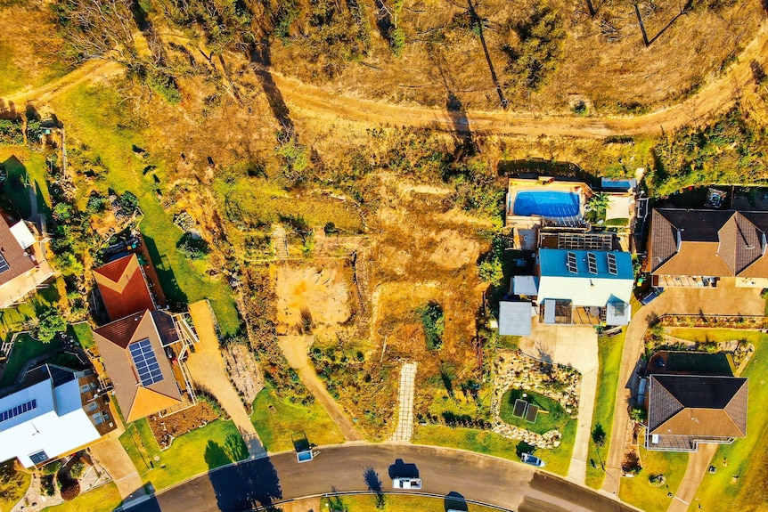 An aerial view of an empty block of land with houses on either side.