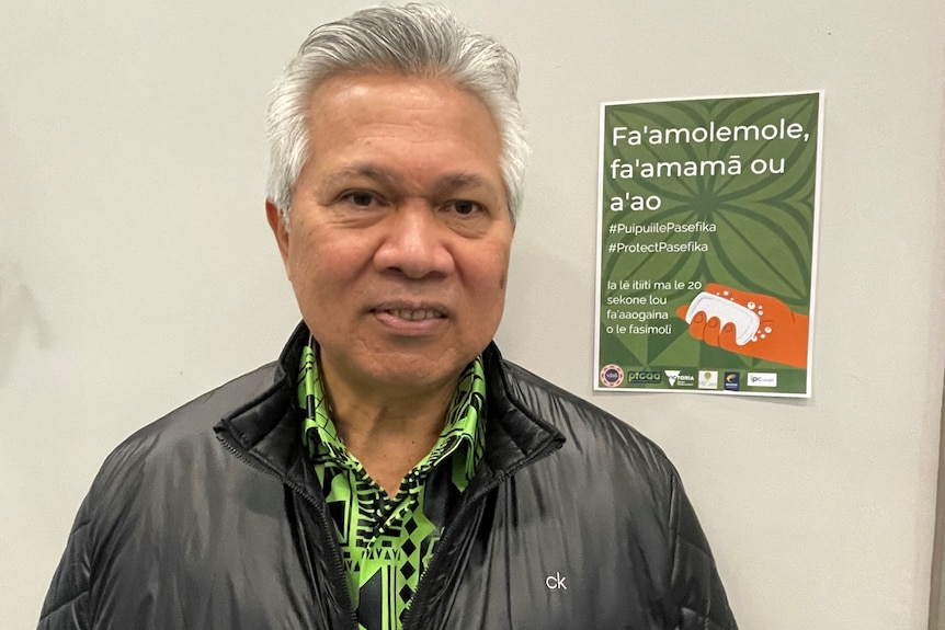 Reverend Aviti Etuale next to a sign with coronavirus information in language.