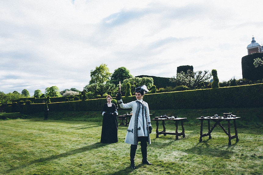 Colour still of Emma Stone and Rachel Weisz standing on lawn in 2018 film The Favourite.