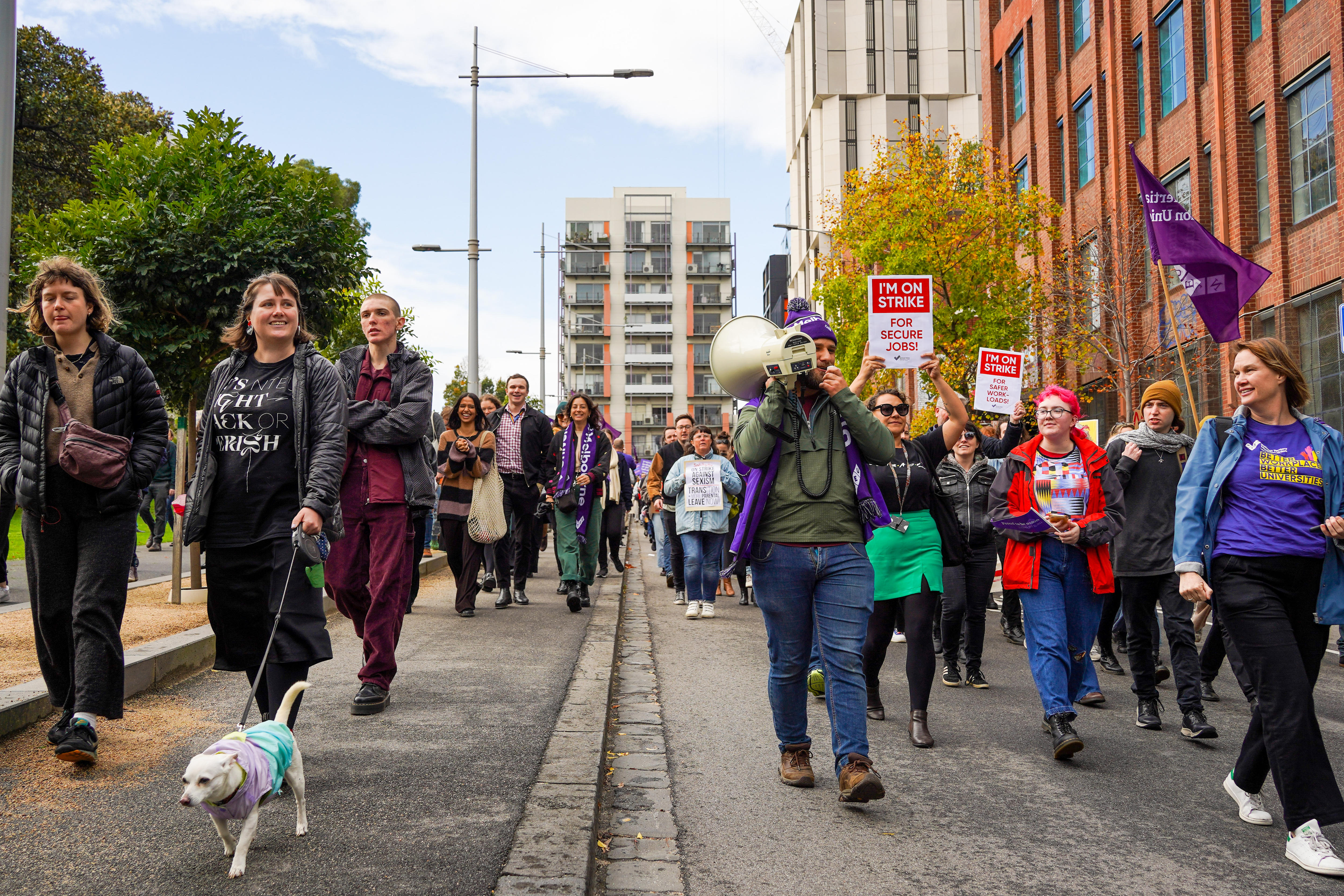University staff march down a street, waving union flags and holding signs that say "I'm on strike!"