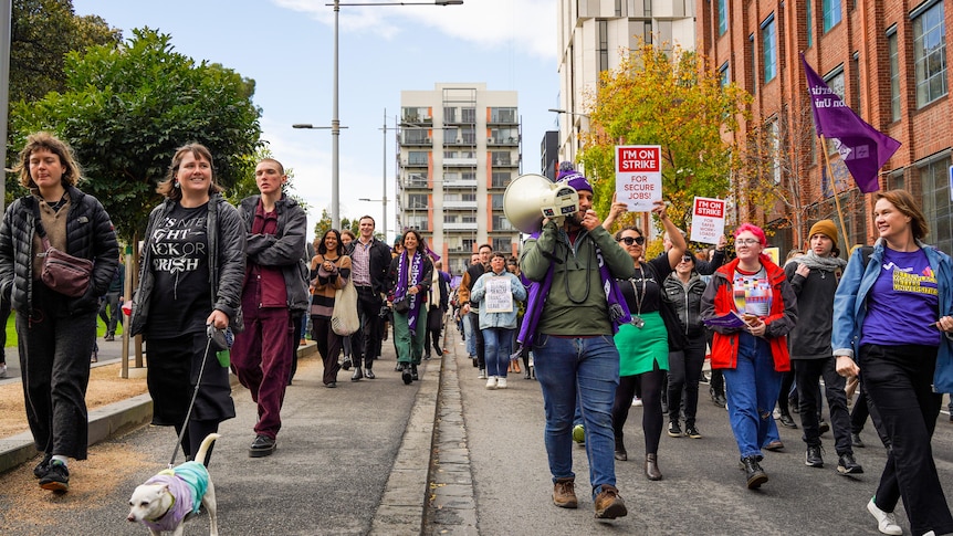 University staff march down a street, waving union flags and holding signs that say "I'm on strike!"