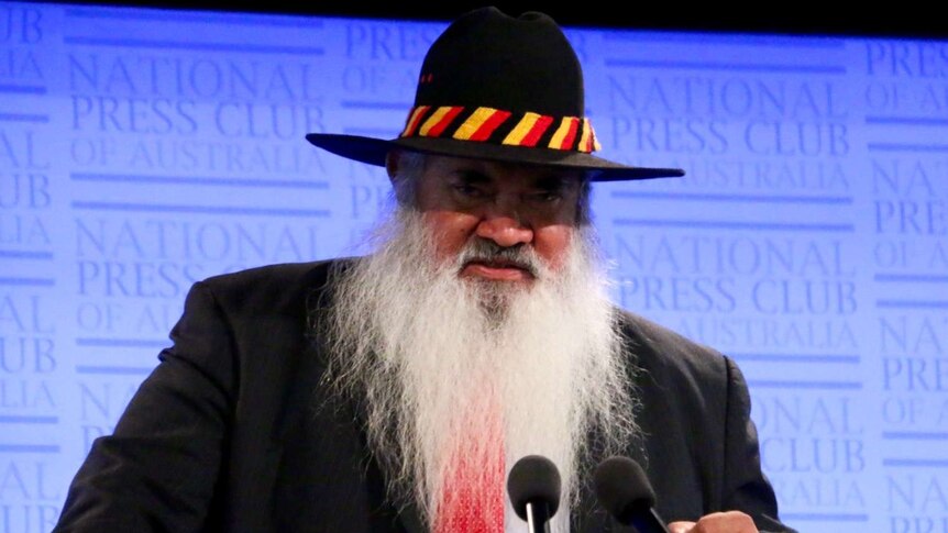 Pat Dodson wears a hat while standing at a lectern