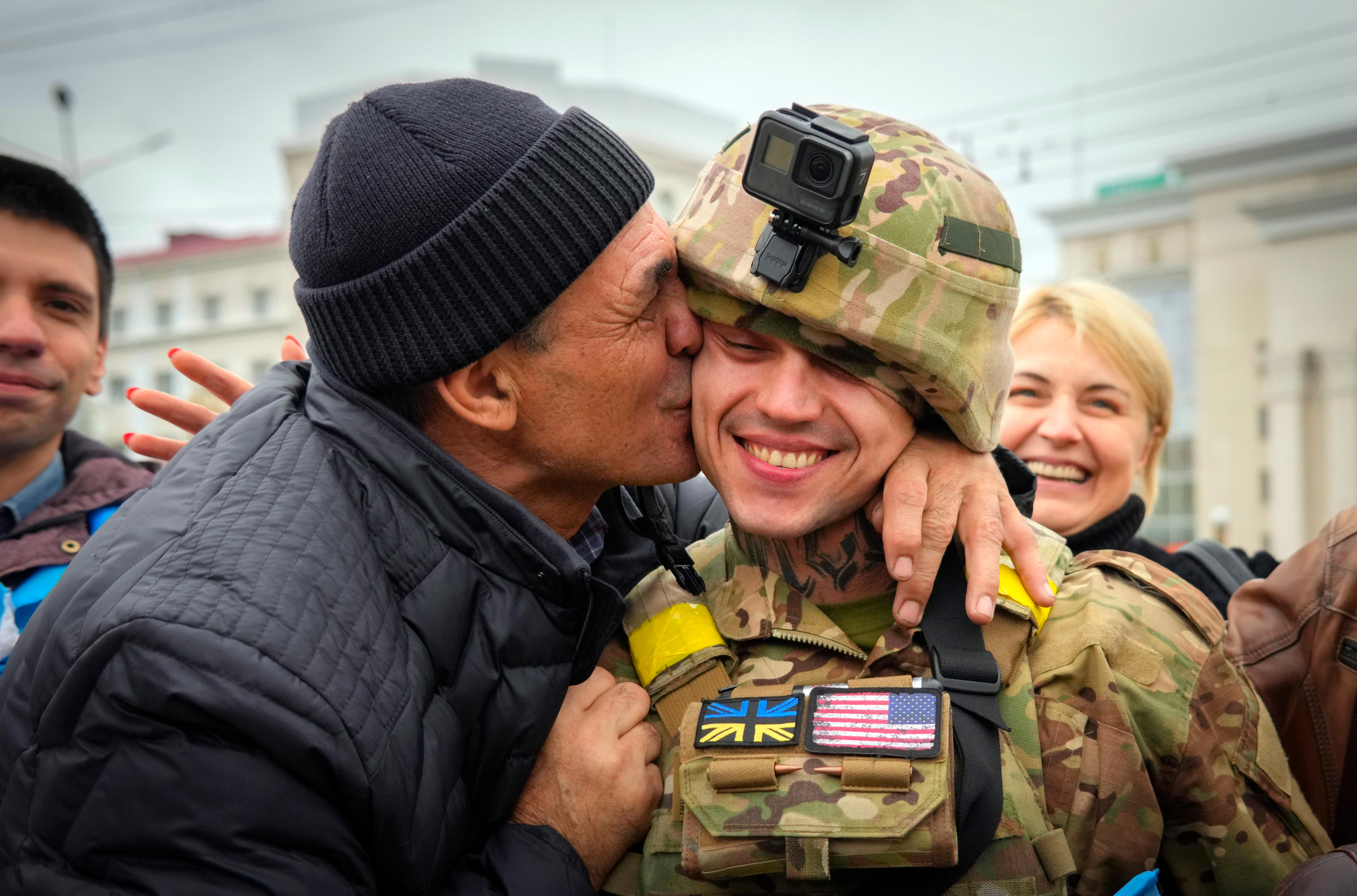 A man kisses a soldier in uniform on the cheek. 