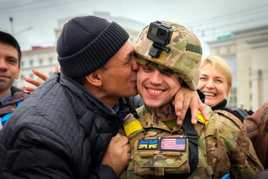 A man kisses a soldier in uniform on the cheek. 