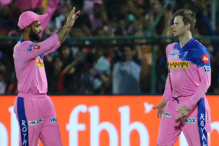 A cricketer raises his hands to high five a teammate who has just taken a catch.