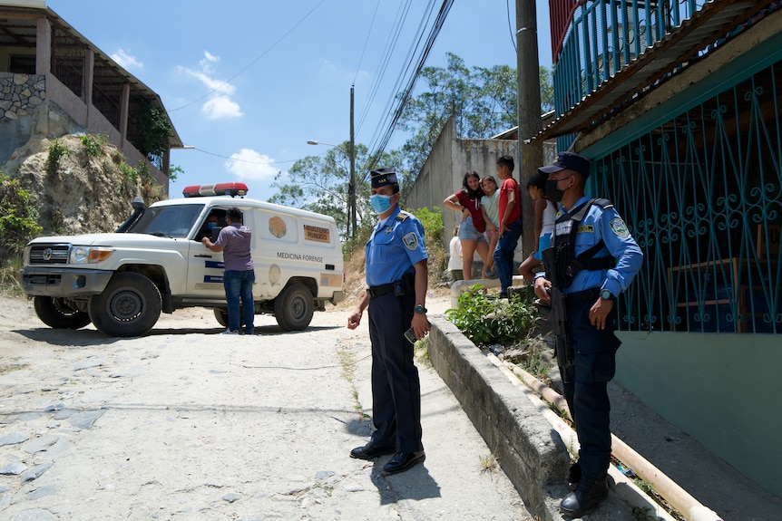 Police stand in front of a police car.